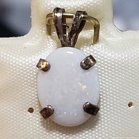 Close-up front view of oval white opal pendant set in sterling silver with four prongs and a silver bail.