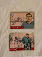 Front of two 1968-69 O-Pee-Chee hockey cards showing Lou Angotti and Earl Ingarfield in Pittsburgh uniforms with action illustration background.