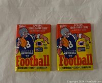 Front view of two unopened 1989 Topps Football packs showing colorful packaging with football player graphic and text detailing contents.