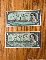 Front side of two Canadian $1 dollar bills with Queen Elizabeth II portrait and Centennial of Canadian Confederation 1867-1967 text.