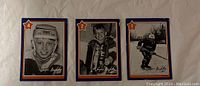 Front view of three 1982-83 Neilson Wayne Gretzky hockey cards numbered 4, 2 and 1, showing black and white images of Gretzky in different youth hockey scenes, with blue, red and orange star accents in corners.