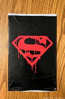 Front view of sealed comic set bag showing red dripping Superman emblem on black background.