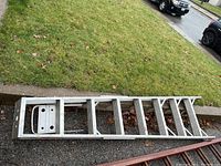 Full view of aluminum step ladder laid horizontally on pavement.