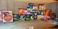 Wide view of shelf with assorted boxed bulbs and burner savers, showing brands NOMA, GE, Stuart House, Econo-Lite, and others.