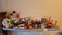 Wide view of Christmas decorations on table including plates, candles, ornaments, cards, and wrapping paper.
