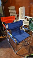Photo showing front view of blue Coleman camping chair with metal frame and fabric seat, and orange Coleman chair behind.