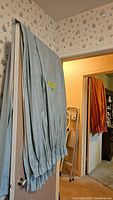 Two sets of light blue linen curtain panels hanging on a door. Panels have pleated bottom detailing.