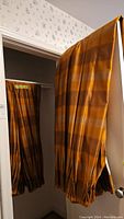 Full view of larger curtain panel set hanging, showing brown and orange stripes and pleated bottoms