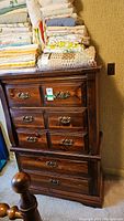 Front view of wood dresser with five drawers showing dark wood stain, ornate metal handles, and textiles stacked on top.