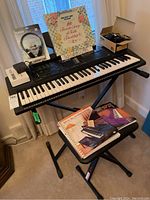 Full setup showing keyboard on stand with stool, headphones box, books and power supply