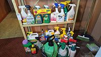 Photo showing assorted garden chemical products and sprayers on a shelf and floor against wood panel wall