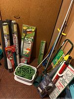 Photo showing garden tools grouped together including weed barrier rolls, Ross Root Feeder, TurfHound Coring Aerator, hose sprayer, and garden hose coiled in container.