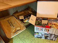 Photo showing Magic Bullet blender set in original box with blender base, multiple containers with colored lids, and recipe books. Phillips electric slicer and wooden board visible in the background.