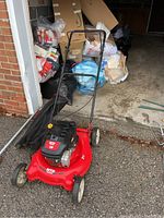Full view of the red MTD lawnmower with attached clippings bag, positioned on outdoor concrete surface near garage.