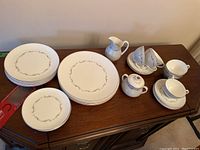 Photo showing the full set arranged including plates, cups, sugar bowl, and creamer on a wooden sideboard.