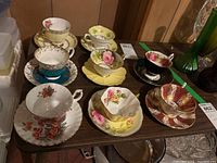 Photo of eight teacups with matching saucers on a wooden surface featuring various floral and decorative patterns.
