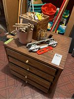 Overview of vintage wooden toolbox with four drawers, and various items on top including wooden pegs, pulleys, and assorted small hardware items.