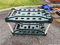 Image of green plastic utility shelf showing top and middle shelves with multiple holes and white supporting legs.