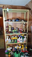 Beige metal utility shelf loaded with various cords, hand tools, spray bottles, and garden items on four shelves