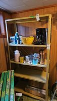 Full view of metal utility shelving unit with household items on shelves including coffee maker, popcorn bowl, and blue iron on top shelf.