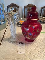 Photo of the clear glass angel sculpture and the red floral glass jar side by side.