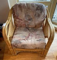 Front and side view of rattan chair showing upholstered seat and back cushions with abstract pattern fabric in muted colors.