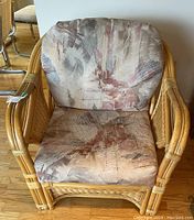 Front view of a rattan chair showing cushioned seat and backrest with muted abstract print upholstery.