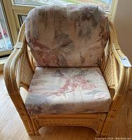 Front view of rattan chair with patterned cushions in window-lit room.