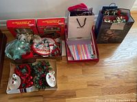 Photo showing boxed Christmas decorations, artificial florals, gift bags, and wrapping paper laid out on hardwood floor.