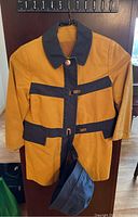 Full view of the girls Westminster raincoat in mustard yellow with black/navy blue collar and trim, showing toggle closures and belt.