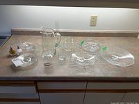 Wide view of the glassware on counter showing pitcher, bowls, trays, cups, and salt and pepper shakers