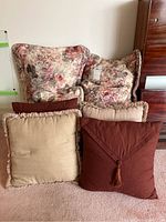 Four cushions and four Croscill floral pillow shams with pillows, arranged together showing variety in color and style.