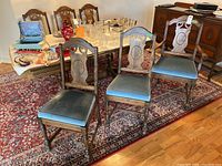 Front view of six wood dining chairs with blue nap fabric upholstered seats positioned in front of a table with various items on it.
