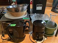 Photo of kitchen appliances and assorted bowls and plates including the coffee maker, kettle, toaster oven, glass jug and ceramic planter.