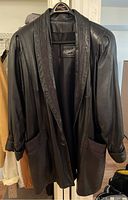 Front view of black leather coat hanging on hanger