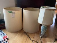 Full view of three lamp shades and lamp on wood floor, showing the size and style of the shades with the lamp