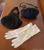 Photo of two black vintage purses and a pair of white gloves arranged on a wooden surface
