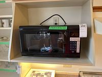 Front view of the black Master Chef microwave oven situated on a white shelf, showing the overall appliance size and design.