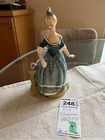 Full view of the Royal Doulton Clarinda figurine on a table, showing figure and small column with bird detail.