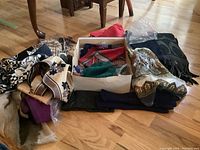 Overview of mixed scarves with different colors and patterns along with folded gloves laid out on floor.