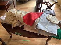 Photo of folded linens, baby clothes including knit caps, and a red cloth piece on a wooden table.