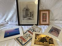 Wide shot showing all art pieces including framed prints, cards, and signed photos laid out on white fabric background.