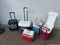 Full group photo of five coolers of various types and sizes sitting upright on a concrete floor in front of a garage door.