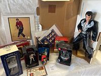 Overview photo of Elvis collectibles including multiple figurines in boxes, framed photo, commemorative stamps, and a large Elvis doll.