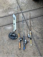 Overview of fishing rods and reels laid on concrete surface, showing fishing rods with attached reels and Garcia Mitchell 300 reel in carrying case