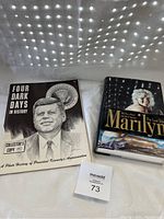 Image showing two books placed on a white cloth background under diffused natural light: 'Four Dark Days in History' with an illustrated cover of President Kennedy, and 'Marilyn: The Last Take' hardcover book with photo of Marilyn Monroe.