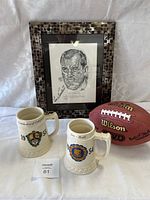 Photo of framed signed art, two ceramic mugs, and football.