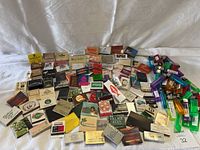 Wide overall photo showing a large collection of vintage matchbooks spread out on a light-colored cloth.