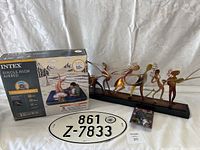 Wide view showing Intex Single-High Airbed box, metal musician figurines on a stand, oval license plate sign, and a small cassette tape.