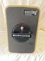 Front view of the Sentry Survivor safe showing the textured black front with beige edges and the circular key lock handle labeled 'SURVIVOR'.